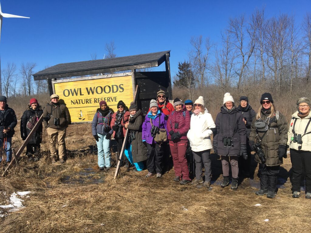 Most of the 25 BirdWing field trip participants posing in the sunshine as the group enters Owl Woods.  This private property has a primary goal of providing a safe roosting place for owls.  Respect for the land and the owls is expected. (Photo: Dean Post)